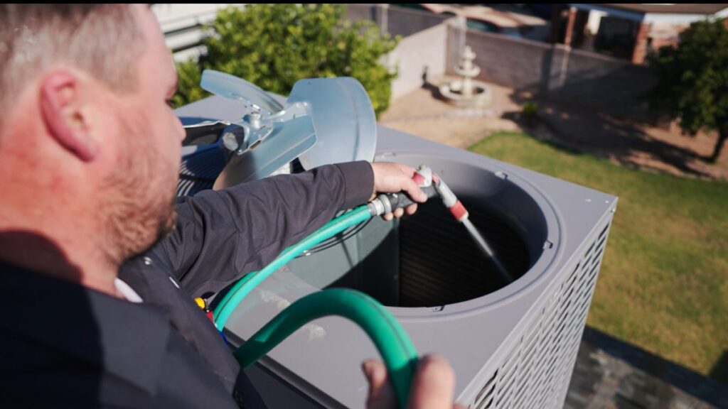 A Sonoran Sun technician rinsing dust off an outdoor condenser coil at a Mesa home