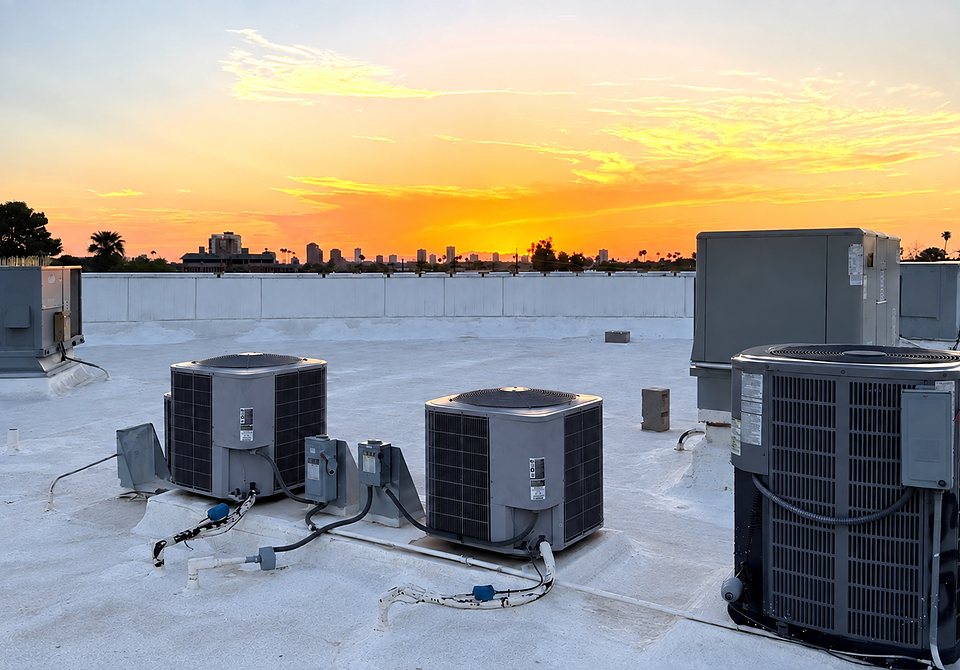 Rooftop condensing units and packaged units on a commercial roof, with the Phoenix skyline at sunset behind them