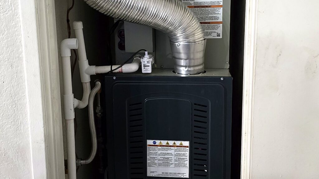 The flue vent and top of a gas furnace in a Mesa hall closet, where dust burns off the first time the heat runs